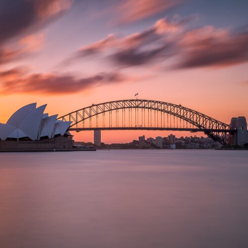 A beautiful shot of the Sydney harbor bridge with a light pink and blue sky in the background at sunset